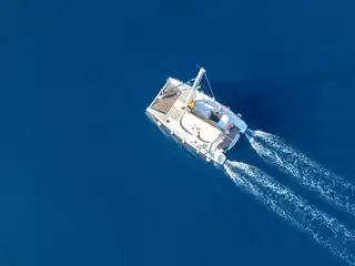Catamaran leaving a white wake across deep blue water, seen from above