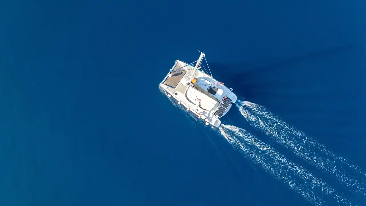 Catamaran leaving a white wake across deep blue water, seen from above