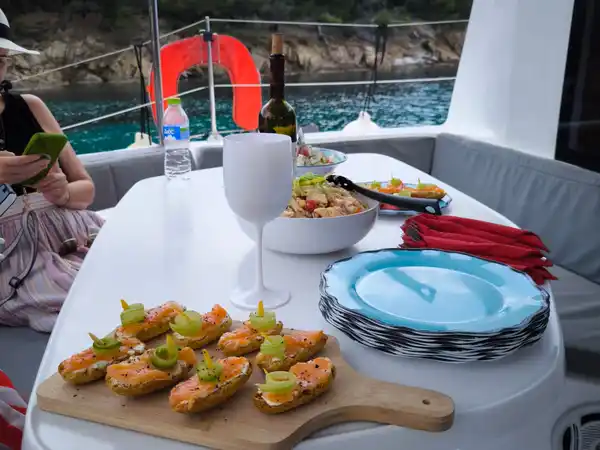 Platter of snacks and drinks on a catamaran table, a pine shore behind