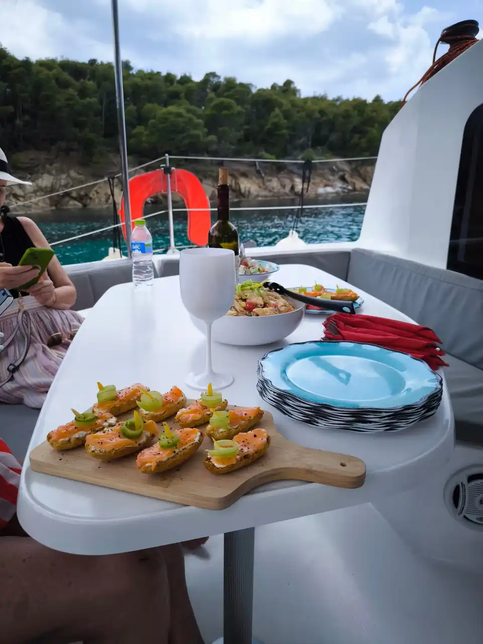 Platter of snacks and drinks on a catamaran table, a pine shore behind