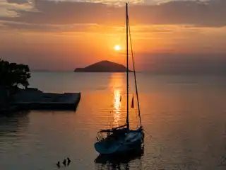 Sailing yacht at anchor at sunset near Porto Carras, a small island on the horizon