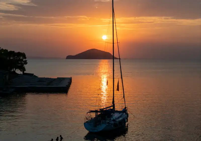 Sailing yacht at anchor at sunset near Porto Carras, a small island on the horizon
