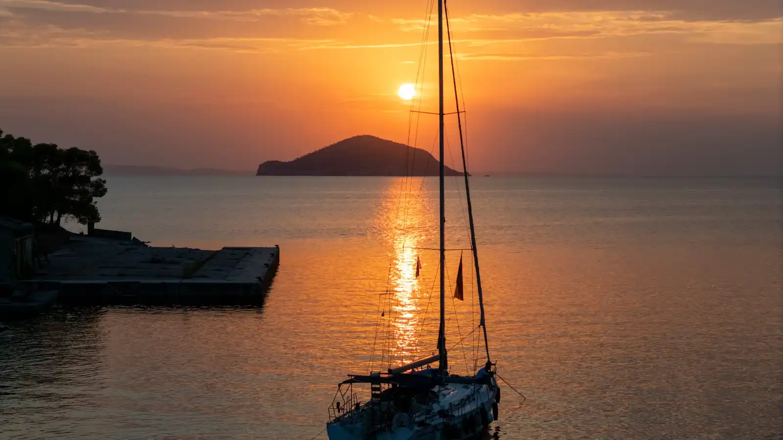 Sailing yacht at anchor at sunset near Porto Carras, a small island on the horizon