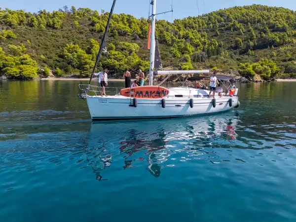 Επιβάτες σε ιστιοπλοϊκό σε ήρεμο όρμο κάτω από πευκόφυτους λόφους, κοντά στο Πόρτο Καρράς