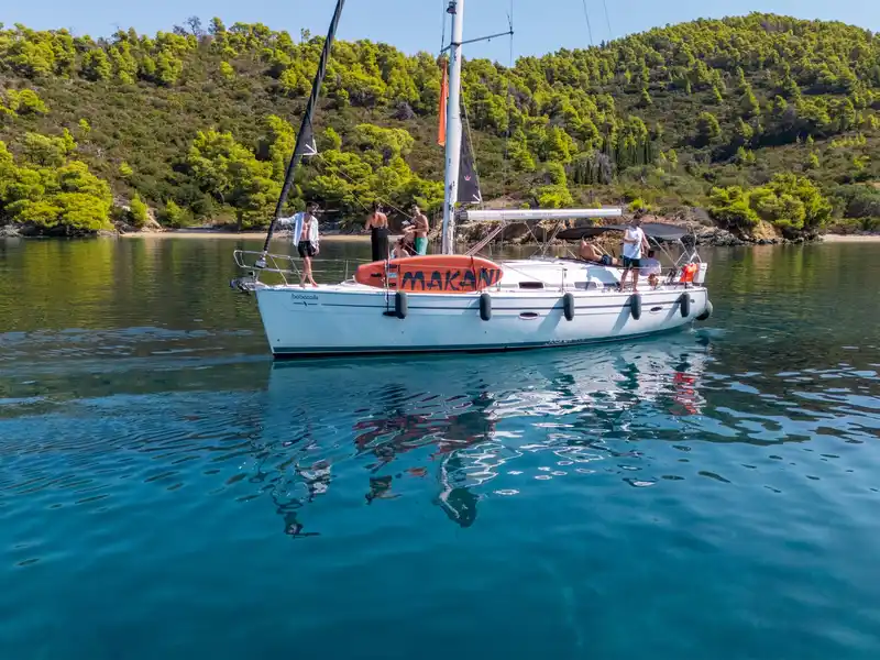 Επιβάτες σε ιστιοπλοϊκό σε ήρεμο όρμο κάτω από πευκόφυτους λόφους, κοντά στο Πόρτο Καρράς