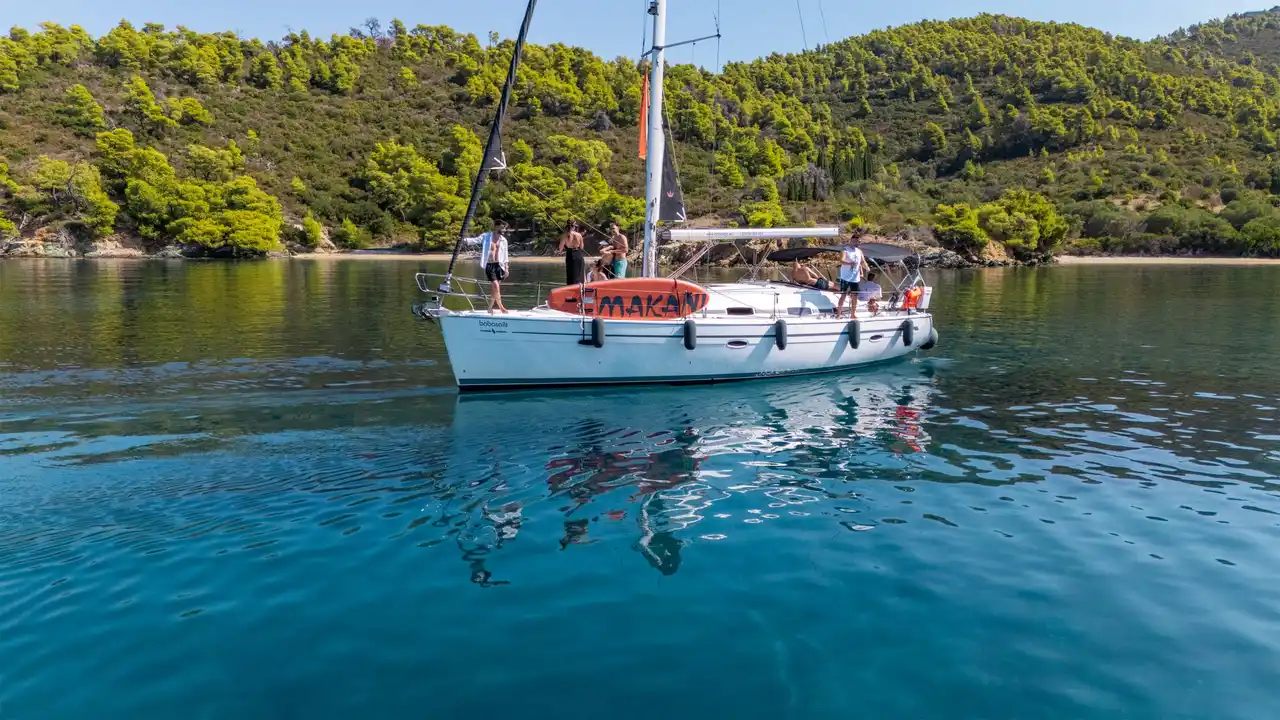 Επιβάτες σε ιστιοπλοϊκό σε ήρεμο όρμο κάτω από πευκόφυτους λόφους, κοντά στο Πόρτο Καρράς