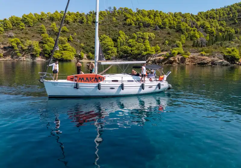 Επιβάτες σε ιστιοπλοϊκό με πορτοκαλί σανίδα SUP, σε ήσυχο όρμο με πεύκα κοντά στο Πόρτο Καρράς