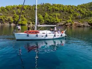 Επιβάτες σε ιστιοπλοϊκό με πορτοκαλί σανίδα SUP, σε ήσυχο όρμο με πεύκα κοντά στο Πόρτο Καρράς