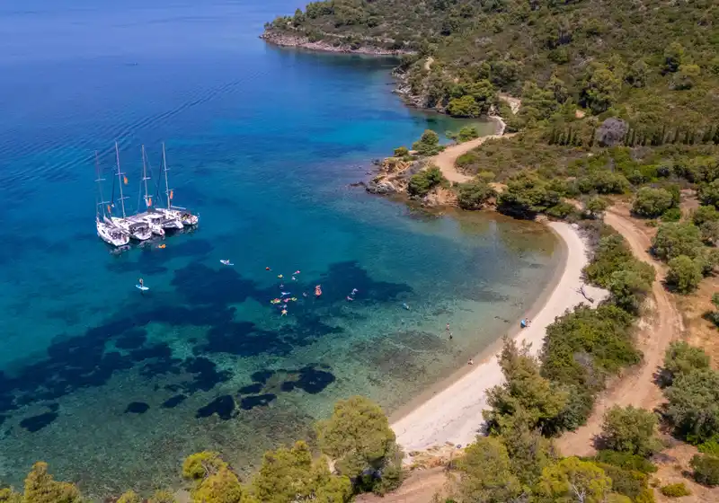 Sailing yachts rafted in a quiet bay near Porto Carras, guests swimming off the beach