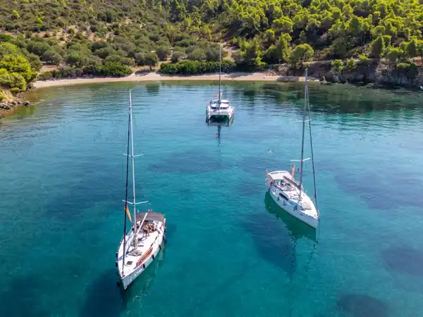 Δύο ιστιοπλοϊκά κι ένα καταμαράν σε τιρκουάζ όρμο κάτω από πεύκα, κοντά στο Πόρτο Καρράς