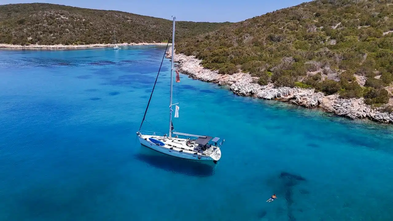 Sailing yacht at anchor in a clear blue cove with a swimmer nearby