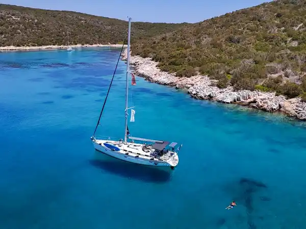 Sailing yacht at anchor in a clear blue cove with a swimmer nearby