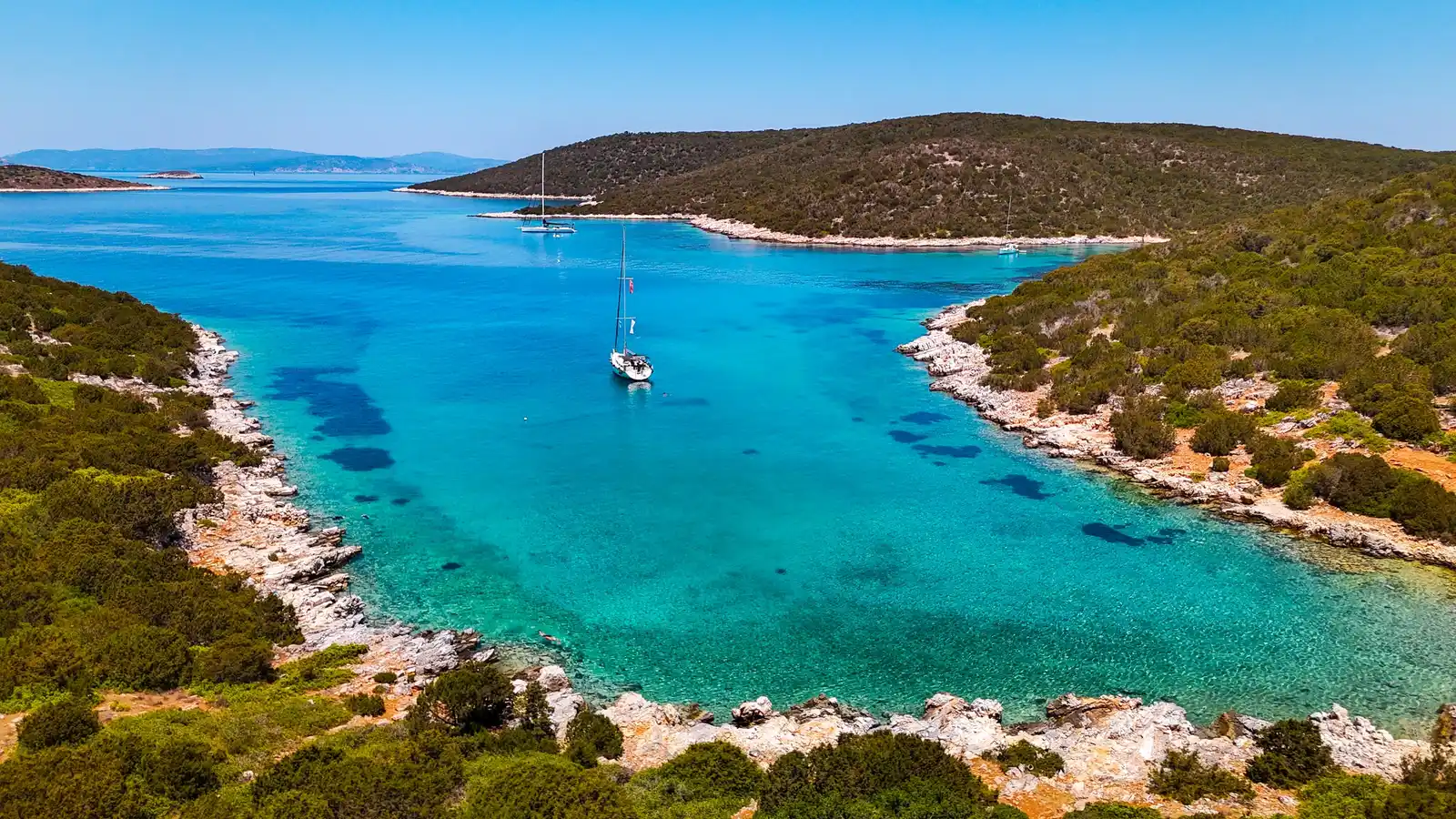 Ιστιοπλοϊκό σε μακρύ τιρκουάζ όρμο ανάμεσα σε χαμηλούς λόφους με θάμνους