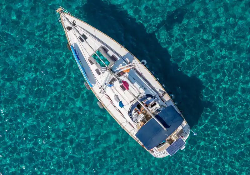 Sailing yacht at anchor over rippled turquoise water, seen from directly above