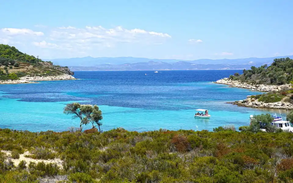 Turquoise cove with a small boat, low shrubs and distant mountains