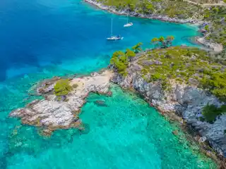 Sailing yachts anchored off a rocky point and turquoise cove at Agnontas on Skopelos