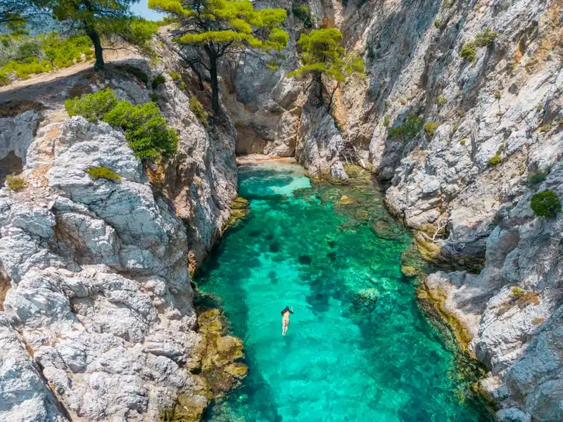 Swimmer floating in a turquoise pool between tall white cliffs on Skopelos