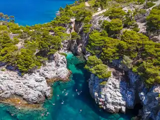 Swimmers in a turquoise inlet below white cliffs and pine forest on Skopelos