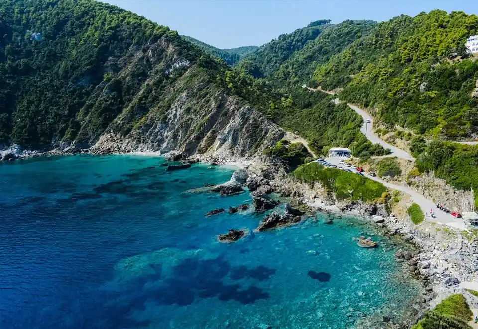Green hills dropping into a turquoise cove, a coast road above
