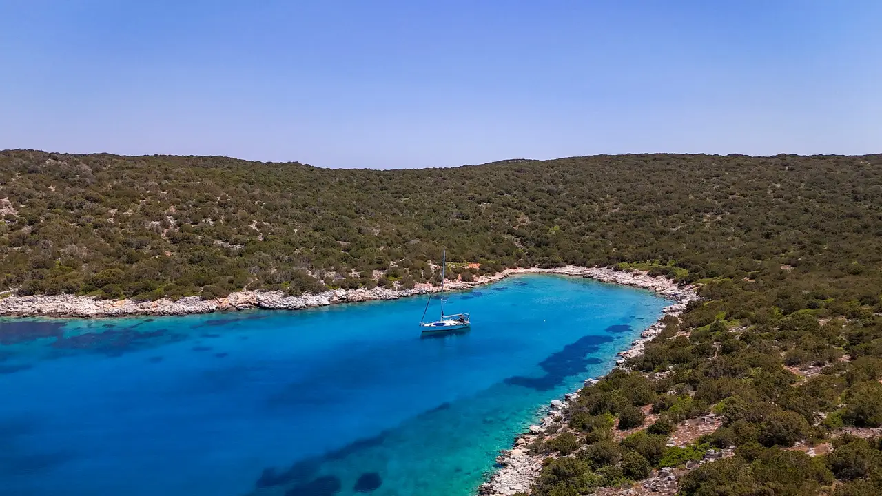 Ιστιοπλοϊκό αγκυροβολημένο σε προφυλαγμένο γαλάζιο όρμο με θάμνους γύρω γύρω, Σποράδες