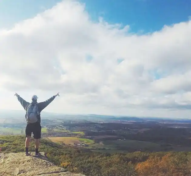 Hiker with raised arms on a rocky summit above a wide valley