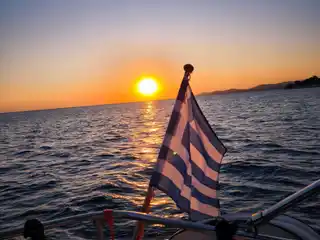 Sun setting over the sea behind a Greek flag on a yacht’s stern