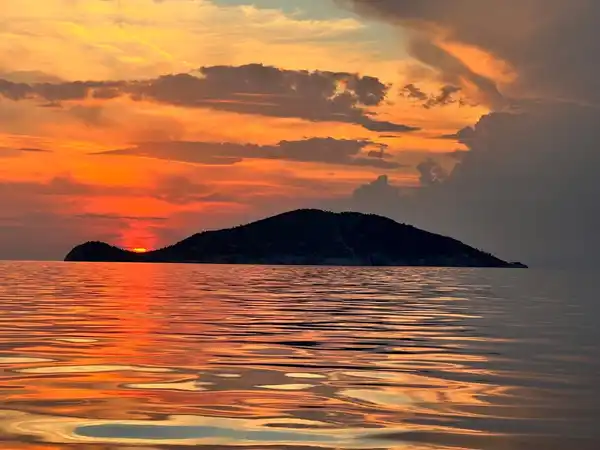 Fiery sunset behind a small island, reflected on rippled water