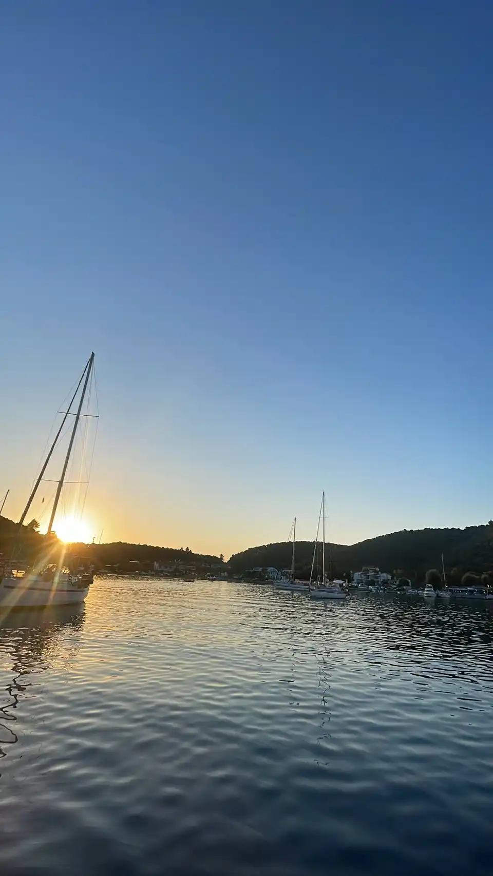Sun setting behind sailing yachts moored in a calm harbour