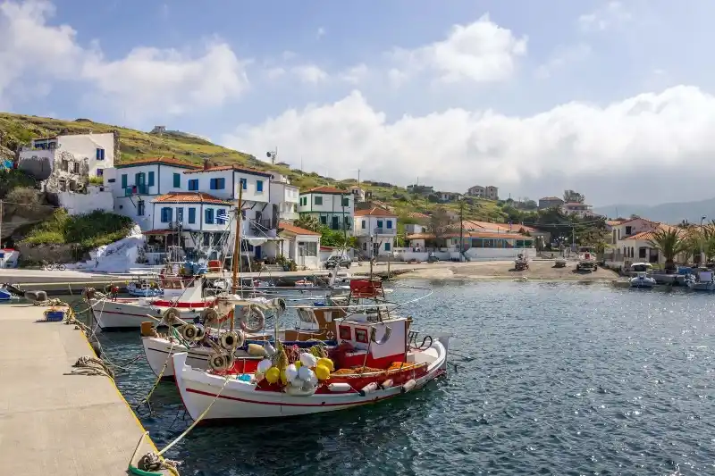 Ψαροκάικα σε μικρό λιμάνι, με άσπρα σπίτια και κόκκινες στέγες στον πράσινο λόφο από πίσω