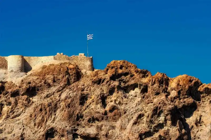 Τείχη παλιού κάστρου με ελληνική σημαία πάνω σε βραχώδη λόφο
