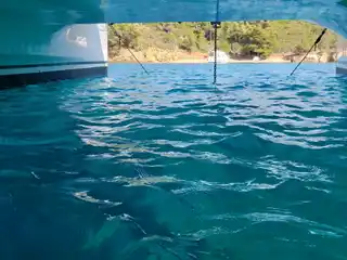 View between the two hulls of a catamaran toward a pine-covered shore