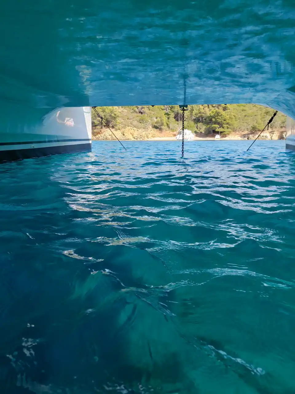 View between the two hulls of a catamaran toward a pine-covered shore