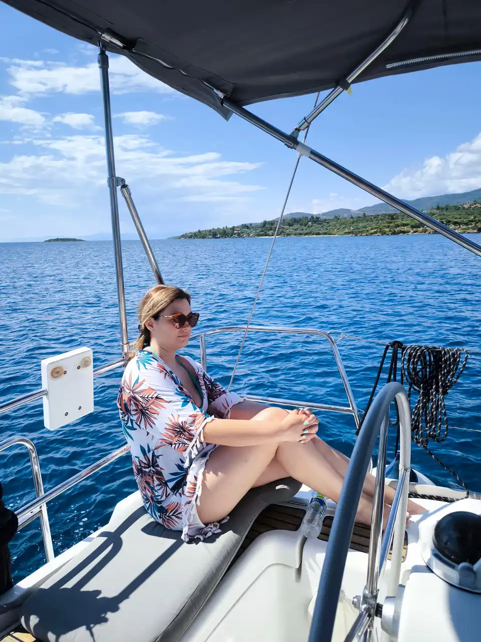 Woman sitting at a sailing yacht’s helm with the coast behind