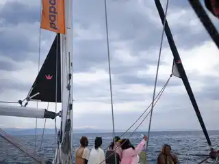 Women sitting on a sailing yacht’s bow under a cloudy sky, a flag on the mast