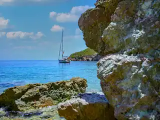 Ιστιοπλοϊκό σε τιρκουάζ όρμο, πίσω από ηλιόλουστα βράχια