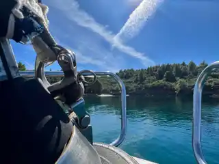 Ropes and a fender on a sailing yacht’s bow, a sunlit pine cove ahead