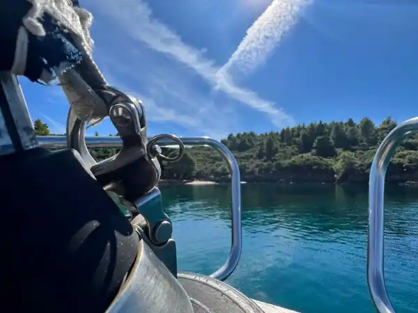 Ropes and a fender on a sailing yacht’s bow, a sunlit pine cove ahead