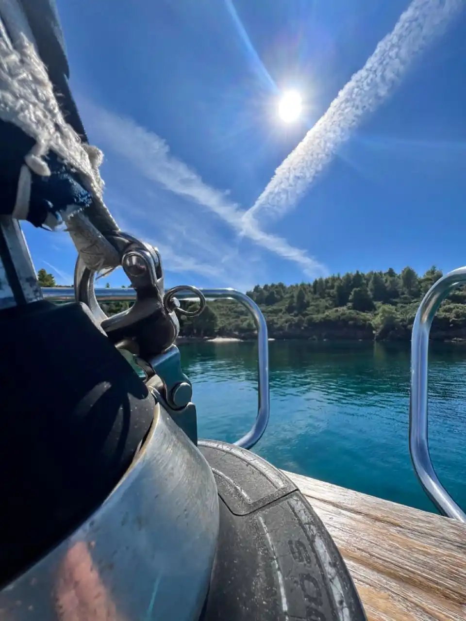 Ropes and a fender on a sailing yacht’s bow, a sunlit pine cove ahead