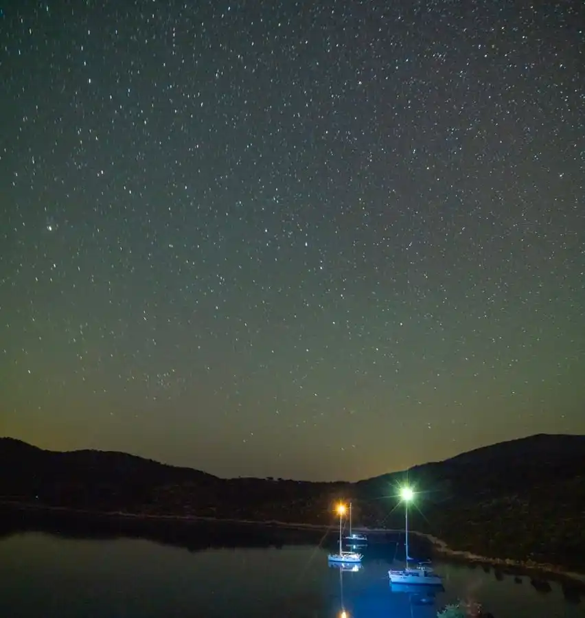 Two yachts lit up in a dark bay under a starry sky